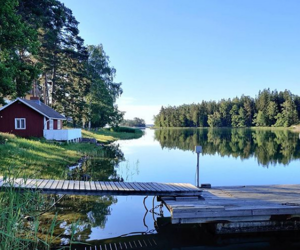 Punainen mökki ja laituri Pensarissa merenrannalla kesän vehreydessä
