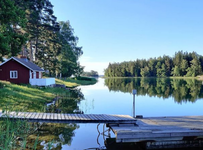 Punainen mökki ja laituri Pensarissa merenrannalla kesän vehreydessä