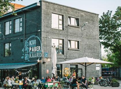 Telliskiven harmaa tiilirakennis ja ihmisiä ulkopöytien ympärille.