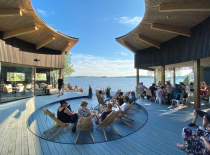 Pistohiekka puinen terassirakennus, ihmisiä tuoleissa, järvi