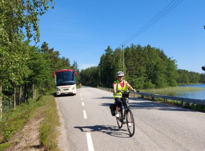 Pyöräilijä maantiellä, bussi ja järvi