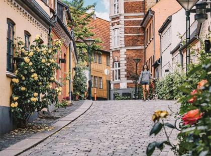 Nainen kävelee Odensen vanhojen kivitalojen ja ruusujen välissä. 